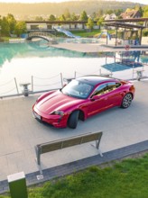 Red sports car parked next to a swimming pool and park bench in daylight, Porsche Taycan, Deer