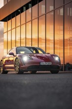 Red sports car reflected in the glass façade of a building at sunset, Porsche Taycan, Deer