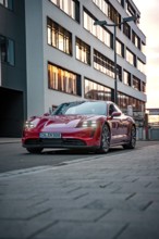 Red sports car parked in front of a modern building in the city at dusk, Porsche Taycan, Deer