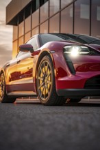 Red sports car reflected in front of a glass façade at sunset, Porsche Taycan, Deer Carsharing,