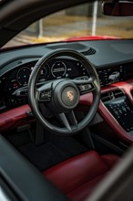 Modern car interior with red and black interior, showing steering wheel and instruments, Porsche