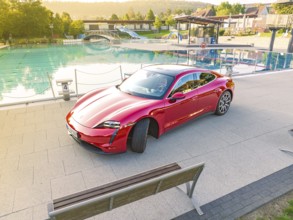 Red sports car next to a swimming pool and park bench in daylight, Porsche Taycan, Deer Carsharing,