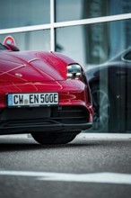 Partial view of the front of a modern red sports car in front of a glass façade, Porsche Taycan,