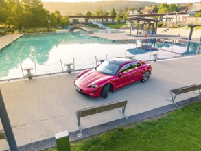Red Porsche Taycan in parking lot next to swimming pool in relaxed landscape, Porsche Taycan, Deer