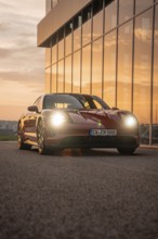 Red car at sunset near a modern building with reflections, Porsche Taycan, Deer Carsharing, Calw,
