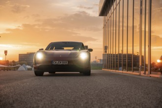 Red car in an urban setting at sunset, reflective windows, Porsche Taycan, Deer Carsharing, Calw,