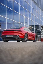 Modern red car in front of a building with glass façade, urban atmosphere, Porsche Taycan, Deer