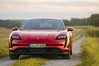 A red sports car on a paved path through rural surroundings at sunset, Porsche Taycan, deer car