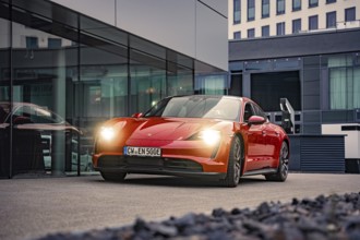 Red car in the city with modern architecture and glowing headlights, Porsche Taycan, deer car