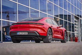 Red car in front of modern architecture with glass facades in the city, Porsche Taycan, Deer car