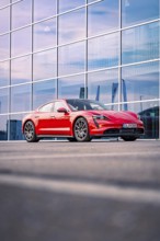 Red sports car in front of a modern building in the evening light, Porsche Taycan, Deer Carsharing.