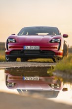 Red car reflected in water on the road at sunrise, Porsche Taycan, Deer car sharing. Calw, Germany