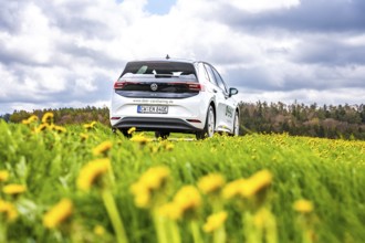 A white car is parked on a flower meadow under a cloudy sky, ID3 VW, deer car sharing. Calw,