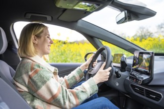 A smiling woman sits in a car and drives through a blooming landscape, ID3 VW, deer car sharing.