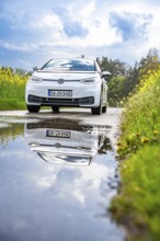 White car on country road, reflected in puddle, surrounded by nature under cloudy sky, ID3 VW, deer