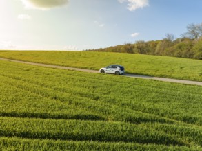 Car on a narrow country road through wide green fields under a sunny sky, ID3 VW, deer car sharing.