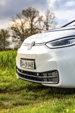 Close-up of a car nose with raindrops on green field in front of trees, ID3 VW, deer car sharing.
