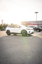 A white car is parked in a parking lot in front of a building at sunset, VW ID4 electric car, Deer