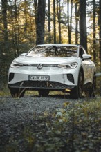 A white car is parked on a gravel path in the forest at dusk, VW ID4 electric car, Deer Carsharing,