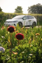 White car in the middle of a blooming meadow under clear sky, natural scene, VW ID4 electric car,