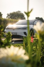 Car behind shiny blossoms in sunlight, warm, glowing depiction of nature, VW ID4 electric car, deer