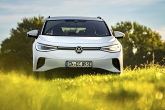 White car in front of green meadow and trees in sunlight, bright, natural scene, VW ID4 electric