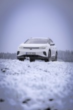 A white car is parked in a snowy field in dull winter weather, VW ID4 electric car, Deer