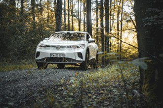 A car is parked in a forest on a path surrounded by autumn leaves and sunlight, VW ID4 electric
