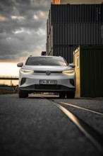 White car drives past container warehouse at sunset, dramatic urban scene, VW ID4 electric car,