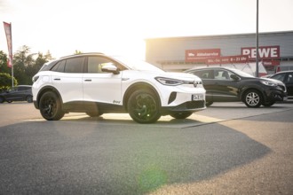 White vehicles in a parking lot in front of a shopping center at sunset, VW ID4 electric car, Deer