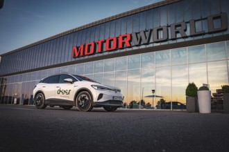 A car stands in front of a large building with glass façade during one evening, VW ID4 electric