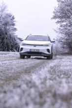 White car in a field with hoarfrost and bare trees in the background, VW ID4 electric car, Deer