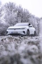 White car in frosty winter landscape with trees covered in hoarfrost, VW ID4 electric car, deer car
