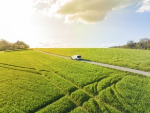 A car drives on a road through a green landscape under a cloudy sky, VW ID4 electric car, Deer