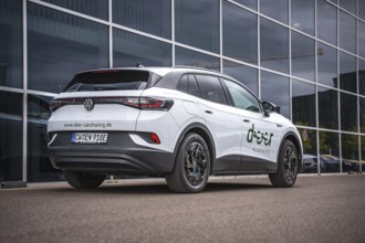 Rear of a white car in front of a modern glass façade in the city, VW ID4 electric car, Deer