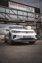 White car under scaffolding at Motorworld with cloudy sky, VW ID4 electric car, Deer Carsharing,