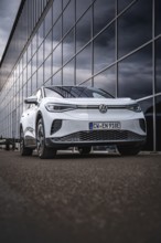 White car in front of a modern glass façade in an urban environment, VW ID4 electric car, Deer
