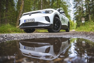 White car in the forest reflected in a puddle on the ground, VW ID4 electric car, Deer Carsharing,