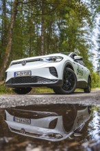 A white car is reflected in a puddle of water on a forest road, VW ID4 electric car, Deer