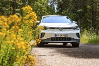 White Volkswagen on a forest road next to yellow flowers, VW ID4 electric car, Deer Carsharing,