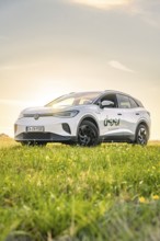 A car is standing in a meadow under a clear sky at sunrise, VW ID4 electric car, Deer Carsharing,