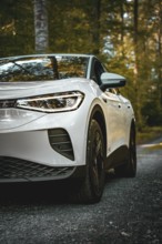 White car in the forest, front view with clear tire display, VW ID4 electric car, Deer Carsharing,