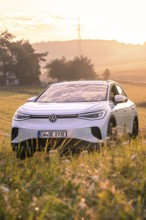 White car in a field at sunrise surrounded by gentle landscape, VW ID4 electric car, deer car