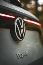 VW logo with rear light of a car in warm light in the forest, VW ID4 electric car, Deer Carsharing,