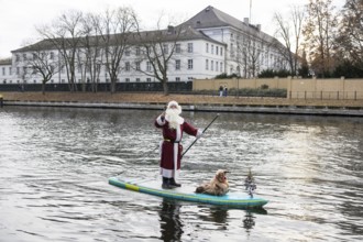 A water sports enthusiast dressed up as Santa Claus rides a SUP on the Spree in front of Bellevue