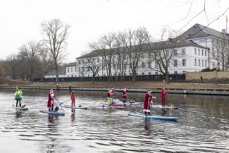 Water sports enthusiasts dressed up as Santa Claus ride SUPs on the Spree in front of Bellevue