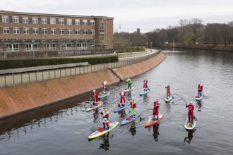 Water sports enthusiasts dressed up as Santa Claus ride SUPs on the Spree am Park at the
