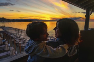 Mother and son embracing warmly while enjoying a breathtaking sunset over the serene waters of