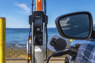 Modern electric vehicle connected to a charging station on the coast with a beautiful ocean view,