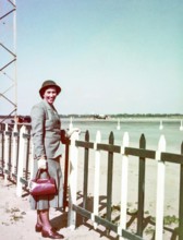 Portrait of smartly dressed woman wearing a suit and hat standing at an airport c 1956